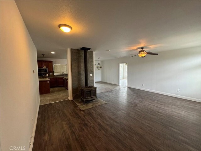 unfurnished living room featuring sink, dark hardwood / wood-style floors, ceiling fan, and a wood stove