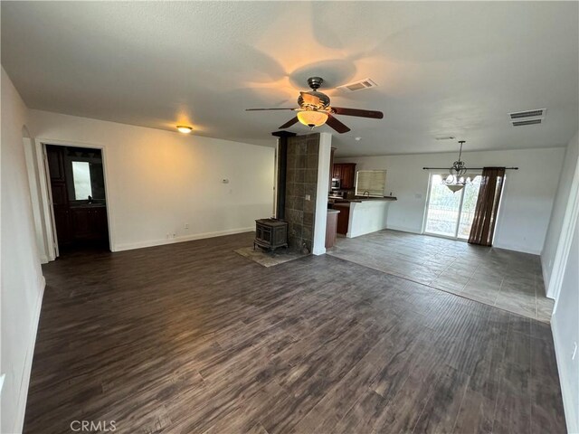 unfurnished living room featuring ceiling fan with notable chandelier, a wood stove, and dark wood-type flooring