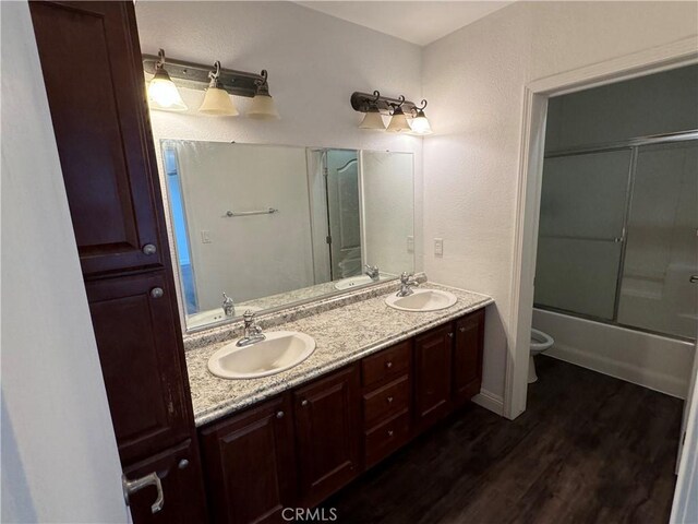 full bathroom with vanity, wood-type flooring, shower / bath combination with glass door, and toilet