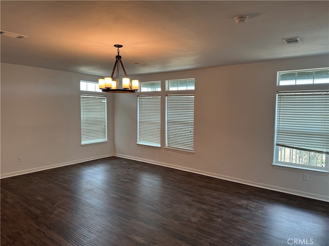 spare room with dark hardwood / wood-style floors and an inviting chandelier