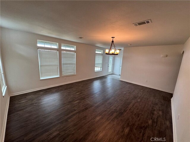 empty room featuring a notable chandelier and dark hardwood / wood-style flooring