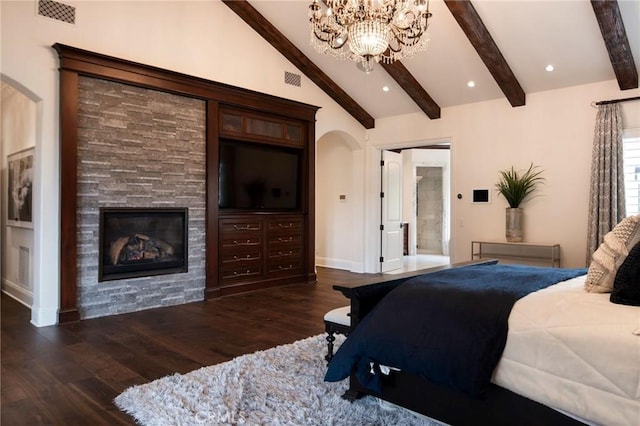 bedroom featuring a stone fireplace, lofted ceiling with beams, dark hardwood / wood-style floors, ensuite bathroom, and a chandelier