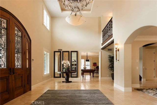 entrance foyer with a tray ceiling, french doors, a high ceiling, and an inviting chandelier