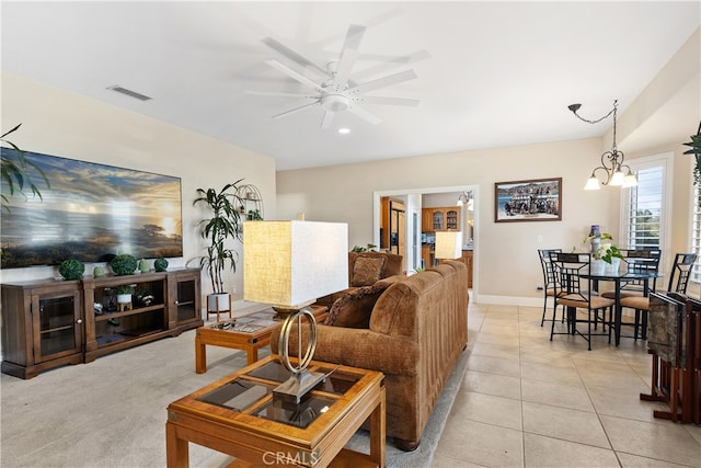 tiled living room with ceiling fan with notable chandelier