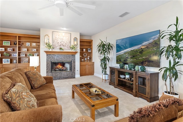 carpeted living room featuring built in shelves, a tiled fireplace, and ceiling fan