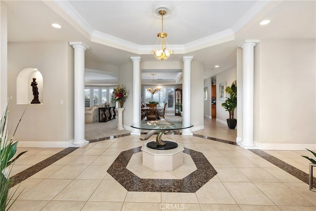 tiled entryway with a raised ceiling, decorative columns, crown molding, and a chandelier