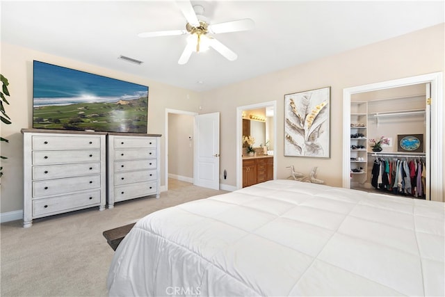 bedroom with ensuite bathroom, ceiling fan, light colored carpet, and a closet