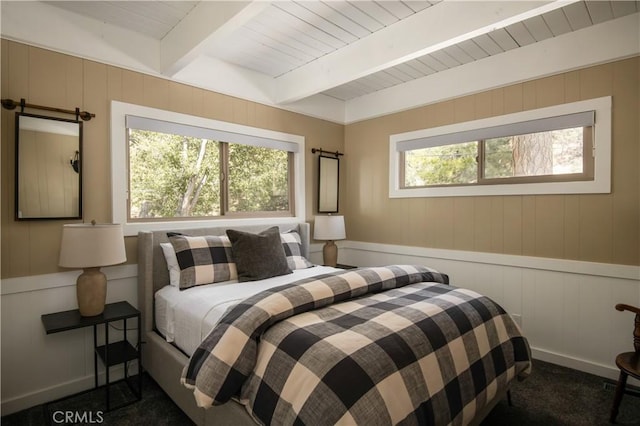 bedroom featuring beam ceiling, multiple windows, wooden walls, and dark colored carpet