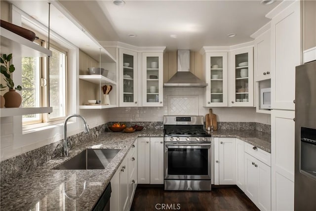 kitchen featuring sink, wall chimney range hood, light stone counters, white cabinets, and appliances with stainless steel finishes