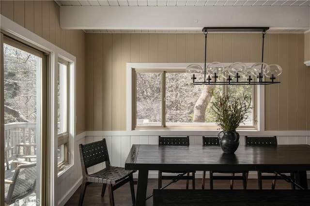 dining area with beam ceiling, wood walls, hardwood / wood-style floors, and a chandelier