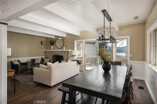 dining area featuring wooden ceiling, dark wood-type flooring, a fireplace, a notable chandelier, and beam ceiling