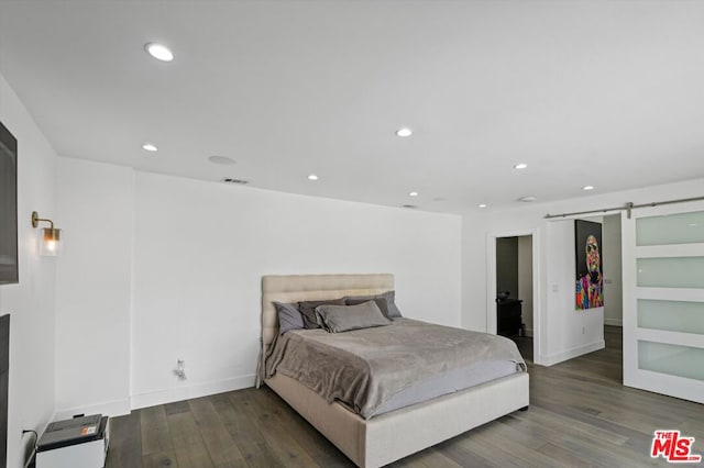 bedroom with a barn door and dark hardwood / wood-style floors