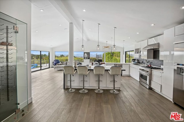 kitchen featuring an island with sink, stainless steel appliances, hardwood / wood-style flooring, vaulted ceiling, and white cabinetry