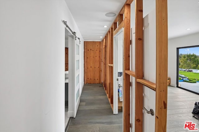 hall featuring wooden walls, light wood-type flooring, and a barn door