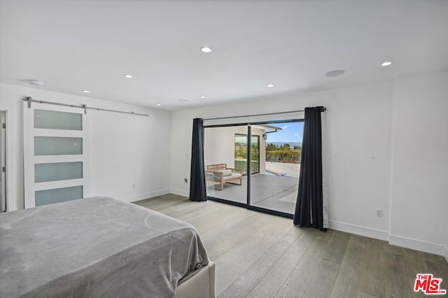 unfurnished bedroom featuring a barn door, access to exterior, and light hardwood / wood-style flooring