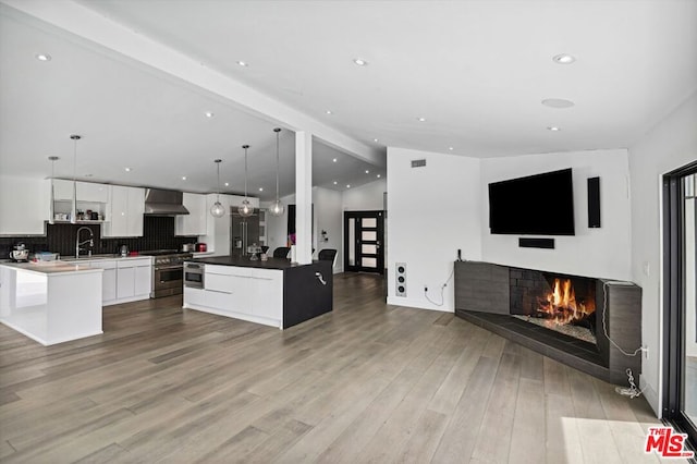 kitchen featuring decorative light fixtures, custom exhaust hood, high end range, white cabinetry, and light wood-type flooring