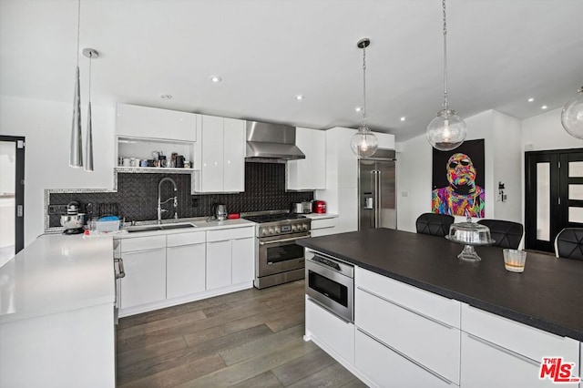 kitchen with pendant lighting, tasteful backsplash, wall chimney range hood, built in appliances, and white cabinetry