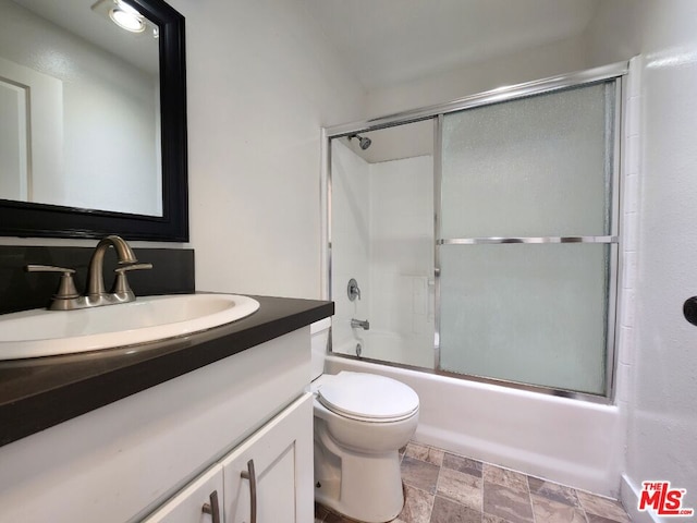 full bathroom with enclosed tub / shower combo, vanity, and toilet