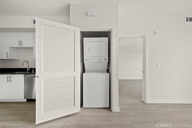 clothes washing area featuring stacked washer and clothes dryer, light hardwood / wood-style flooring, and sink