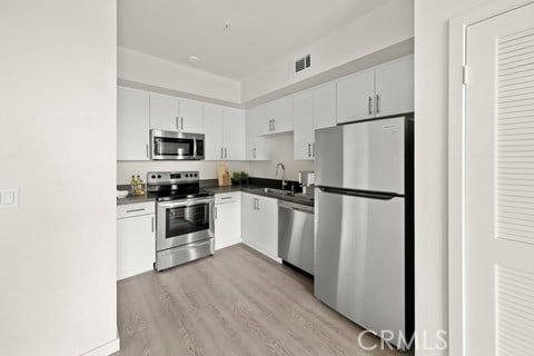 kitchen with white cabinetry, sink, stainless steel appliances, and light hardwood / wood-style flooring