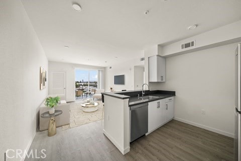 kitchen with hardwood / wood-style floors, sink, dishwasher, kitchen peninsula, and white cabinetry