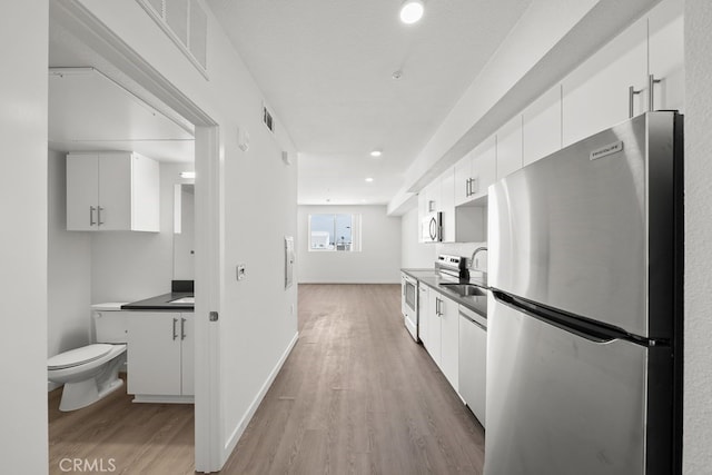 kitchen featuring white cabinets, a textured ceiling, stainless steel appliances, and light hardwood / wood-style floors