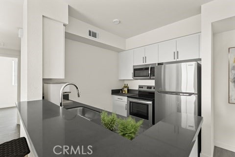 kitchen with hardwood / wood-style floors, white cabinets, sink, kitchen peninsula, and appliances with stainless steel finishes