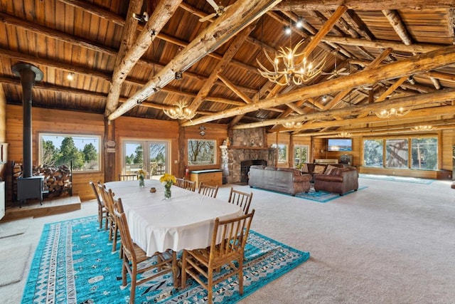 carpeted dining room with a notable chandelier, beam ceiling, wooden ceiling, wooden walls, and a stone fireplace