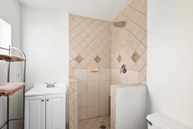 bathroom with toilet, a tile shower, and vanity