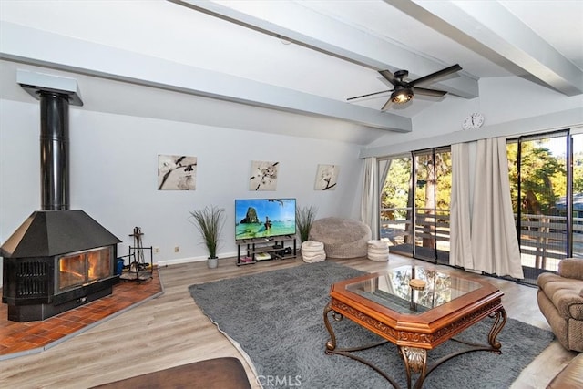 living room with wood-type flooring, lofted ceiling with beams, ceiling fan, and a wood stove