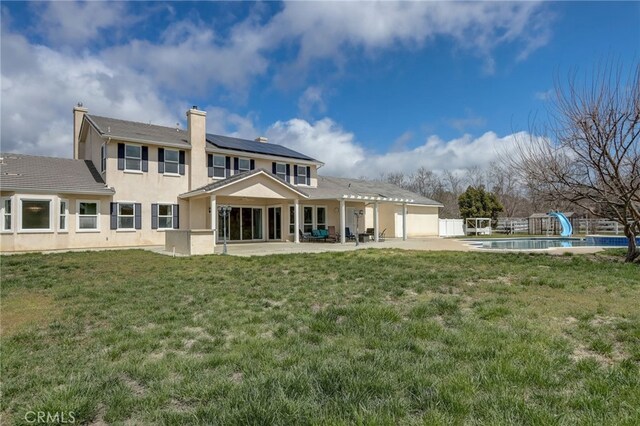 rear view of property with solar panels, a yard, a fenced in pool, and a patio