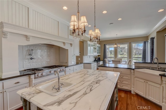 kitchen with sink, hanging light fixtures, a notable chandelier, dark stone counters, and a kitchen island with sink