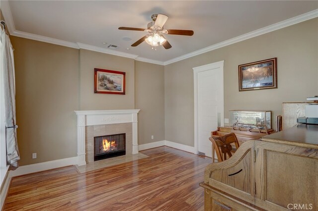 interior space featuring a tile fireplace, light hardwood / wood-style floors, ceiling fan, and crown molding