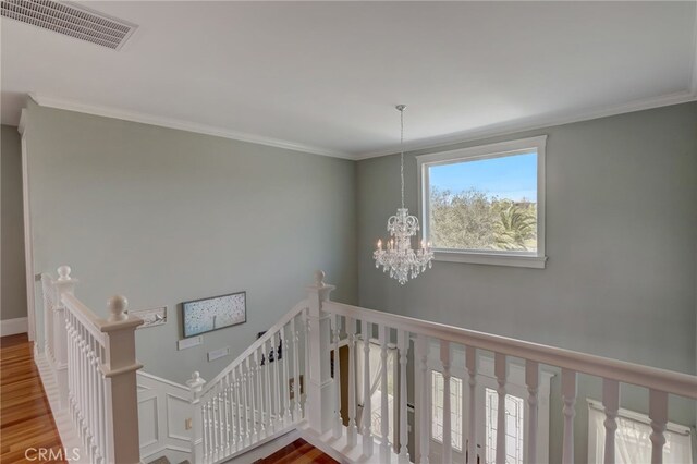 stairway featuring hardwood / wood-style floors, crown molding, and an inviting chandelier