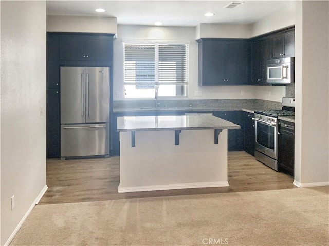 kitchen featuring light carpet, a kitchen island, a breakfast bar, stainless steel appliances, and a sink