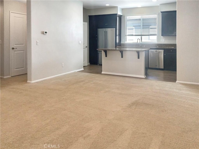 kitchen featuring baseboards, a kitchen bar, appliances with stainless steel finishes, and light colored carpet