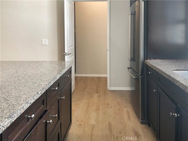 kitchen featuring light stone countertops, light wood-style flooring, baseboards, and freestanding refrigerator