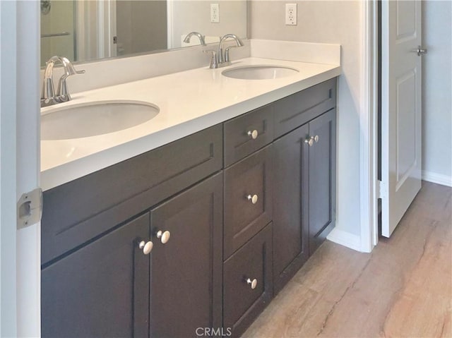 full bathroom with double vanity, a sink, baseboards, and wood finished floors