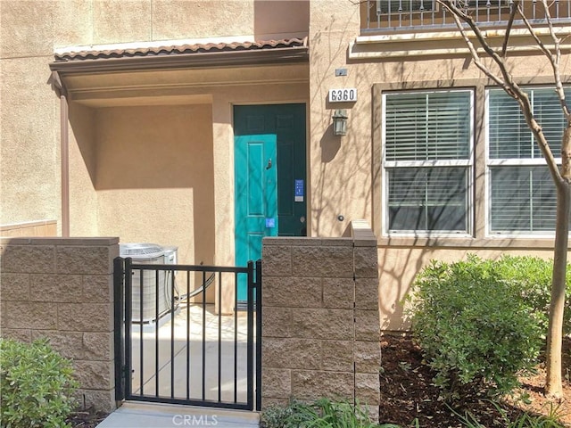 doorway to property with a gate, fence, central AC unit, and stucco siding