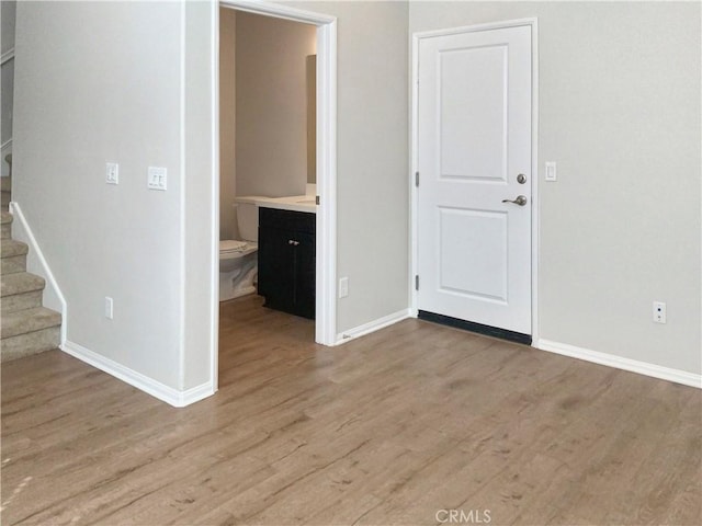 spare room featuring baseboards, stairway, and light wood finished floors