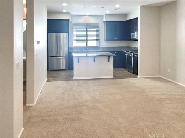 kitchen featuring appliances with stainless steel finishes, light carpet, a kitchen island, and a kitchen bar