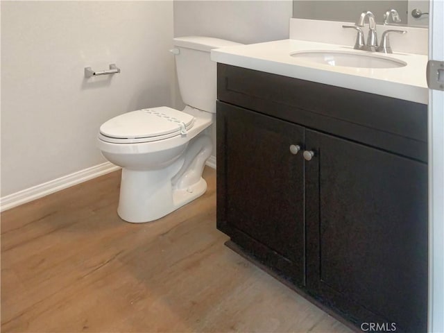 half bath featuring toilet, baseboards, wood finished floors, and vanity