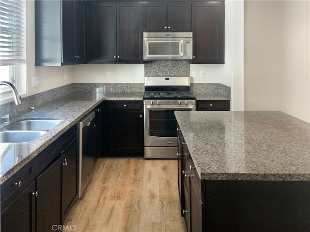 kitchen featuring stainless steel appliances, light wood finished floors, stone counters, and a sink