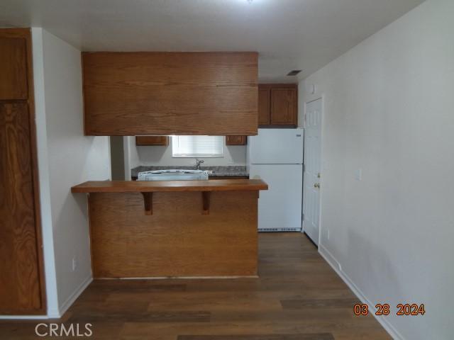 kitchen featuring a breakfast bar area, kitchen peninsula, white fridge, and dark wood-type flooring