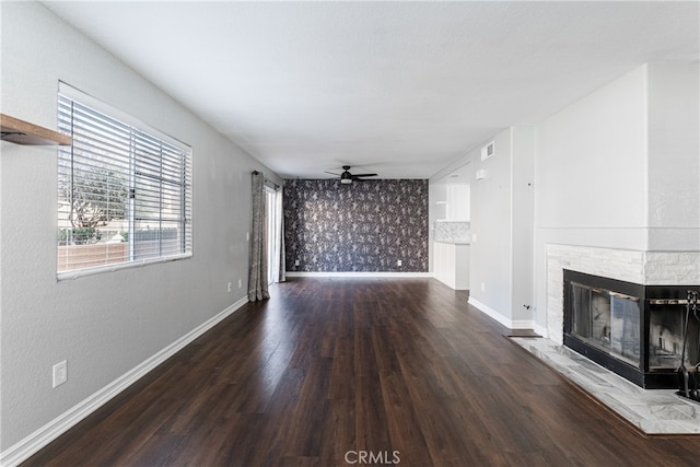 unfurnished living room featuring ceiling fan, a stone fireplace, and dark hardwood / wood-style floors