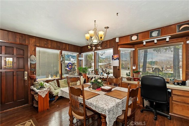 dining space featuring a notable chandelier, wood walls, and dark hardwood / wood-style flooring