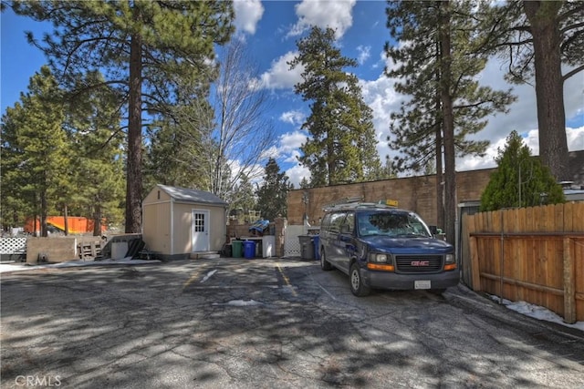 view of car parking featuring fence and a storage unit