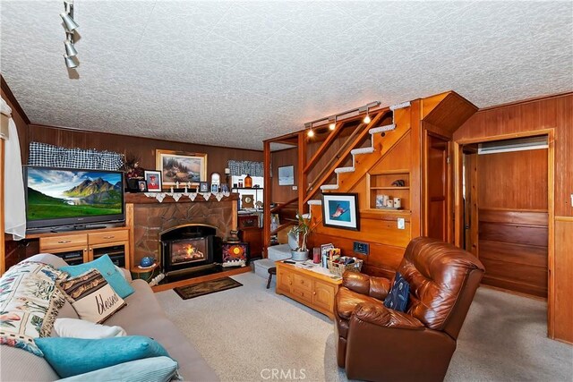 living room with wooden walls, a textured ceiling, carpet flooring, and a stone fireplace