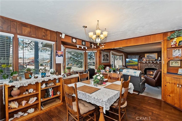 dining room featuring wood walls, a glass covered fireplace, dark wood finished floors, and a notable chandelier