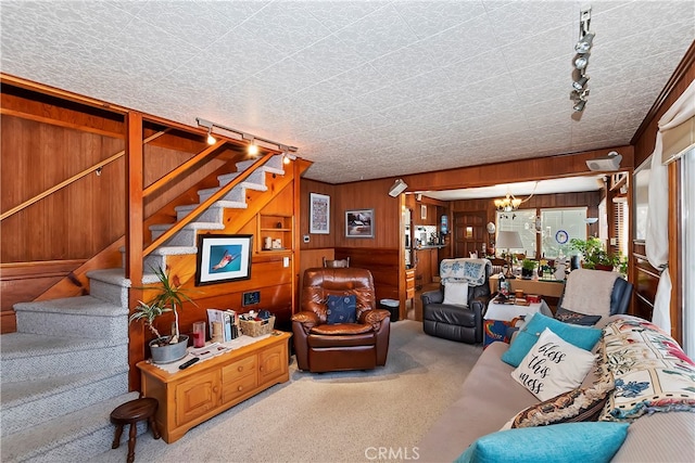 carpeted living room with a textured ceiling, wooden walls, and track lighting